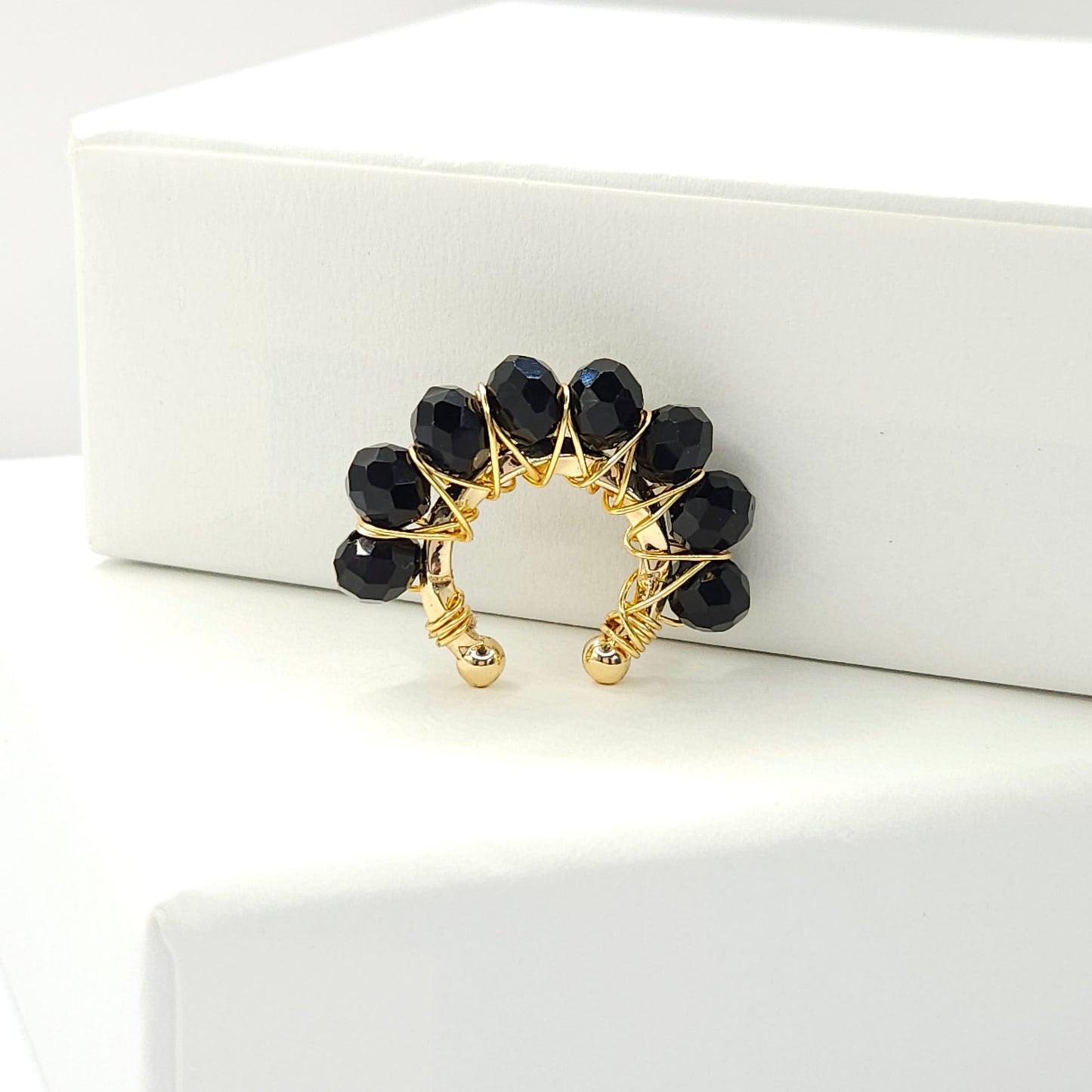 Golden ear cuff adorned with a delicate weave of black faceted rondelle glass beads standing on a white base