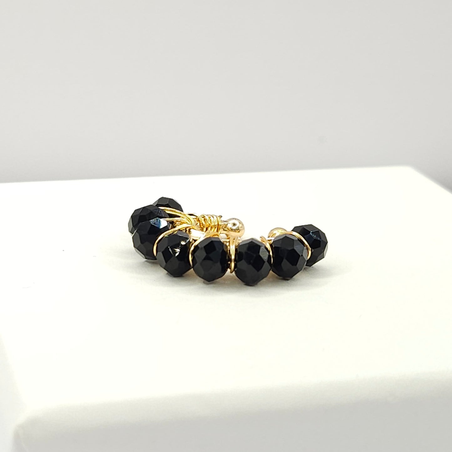 Golden ear cuff adorned with a delicate weave of black faceted rondelle glass beads lying on a white base