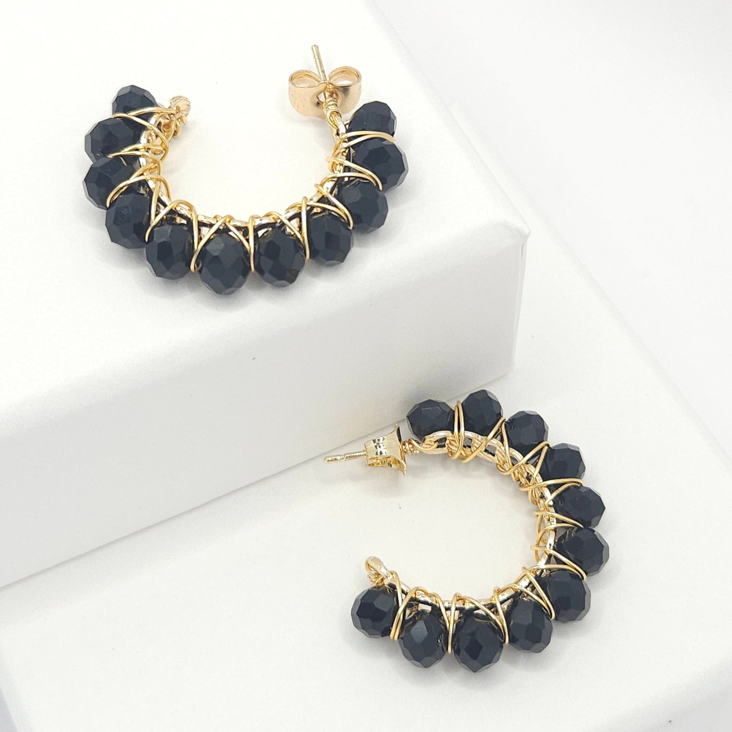 Golden hoops with delicate black faceted rondelle glass beads, both lying on white bases