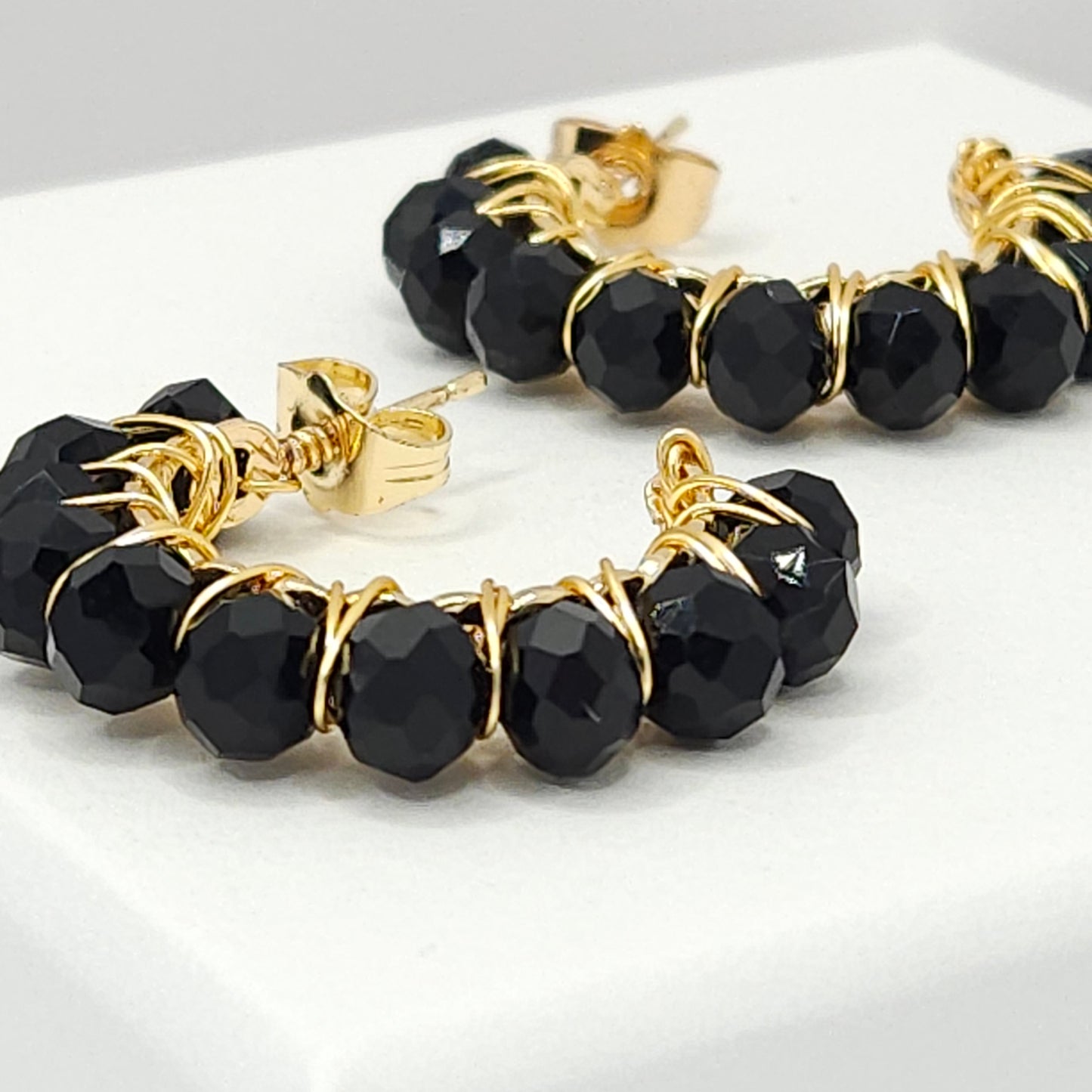Close-up of golden hoops with black faceted rondelle beads, focused on lower left details, blurring towards upper right corner