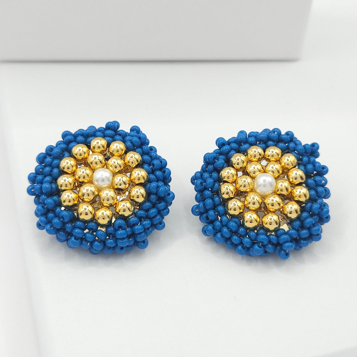 Large stud earrings with a round shape, adorned with blue Czech beads, goldtone spheres, and a pearl at their centre