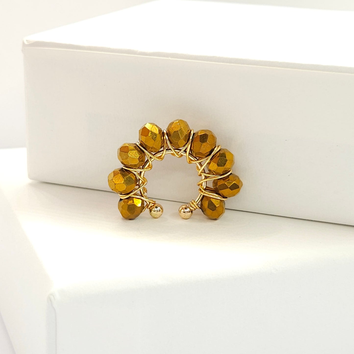 Golden ear cuff adorned with a delicate weave of chocolate faceted rondelle glass beads standing on a white base