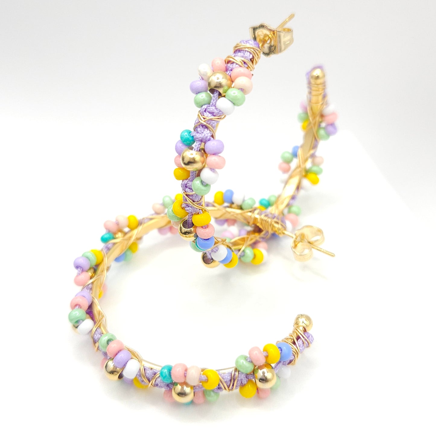 Golden hoops with soft pastel Czech beads, intertwined, one lying on a white base and the other one standing