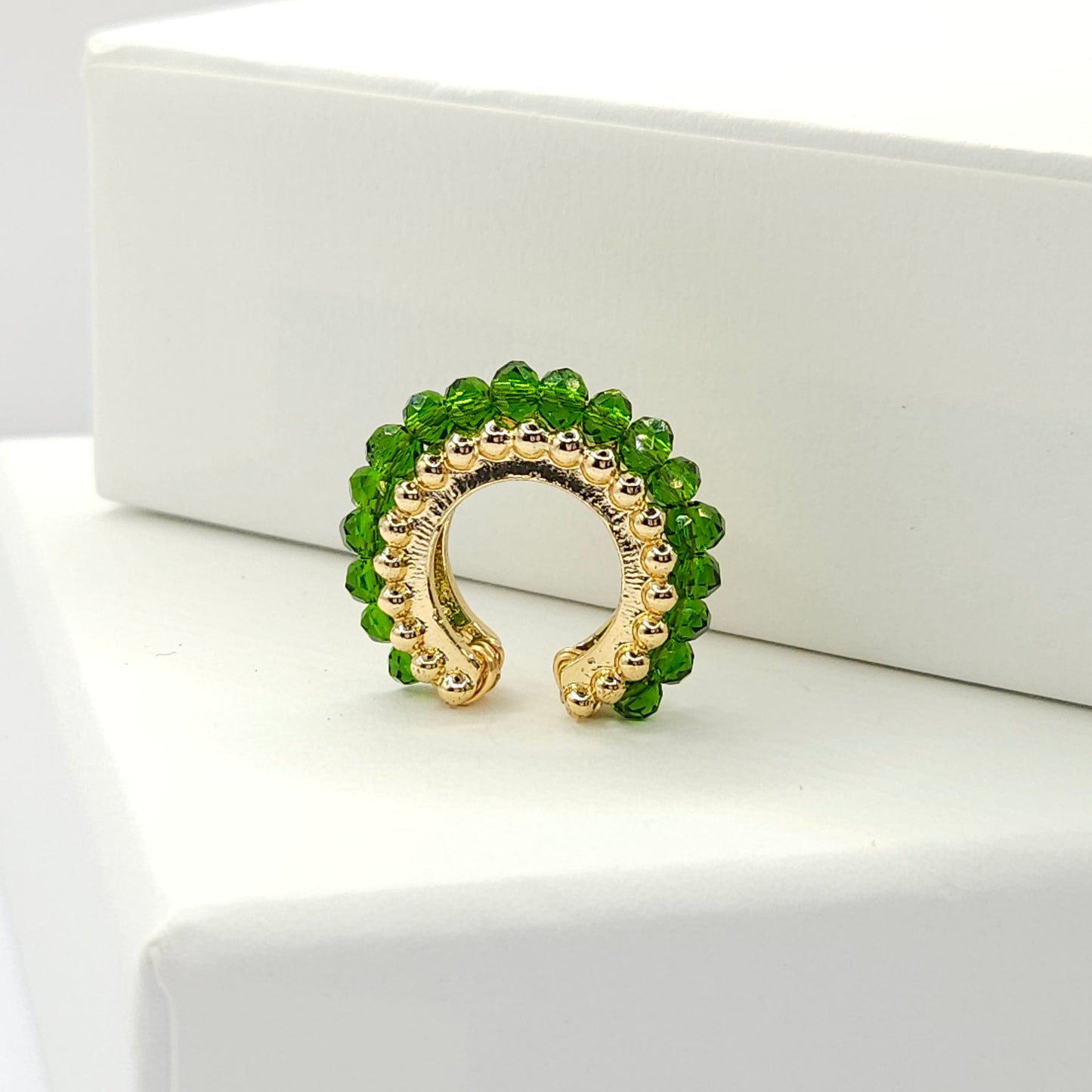 Golden ear cuff featuring an array of green faceted rondelle glass beads standing on a white base
