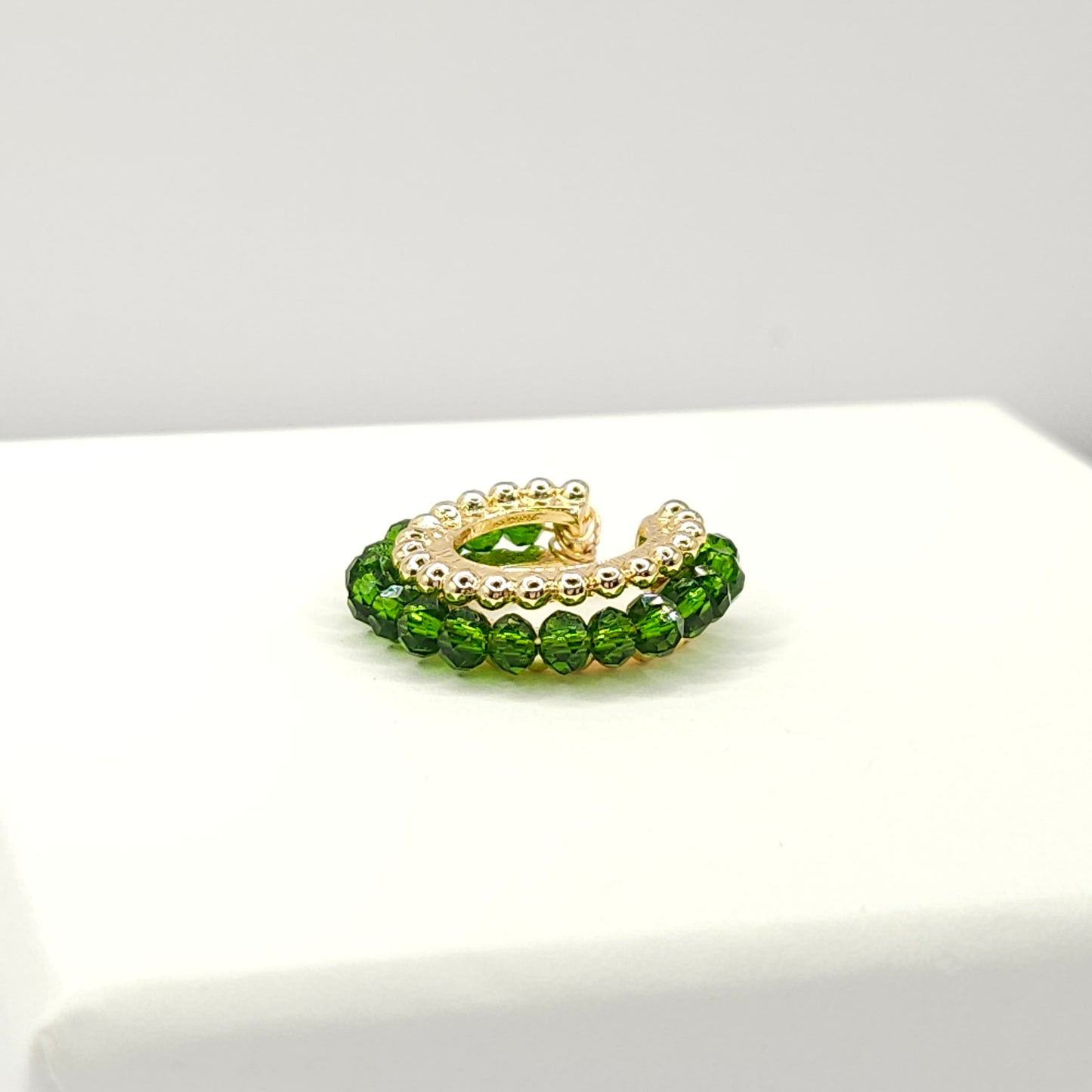 Golden ear cuff featuring an array of green faceted rondelle glass beads lying on a white base