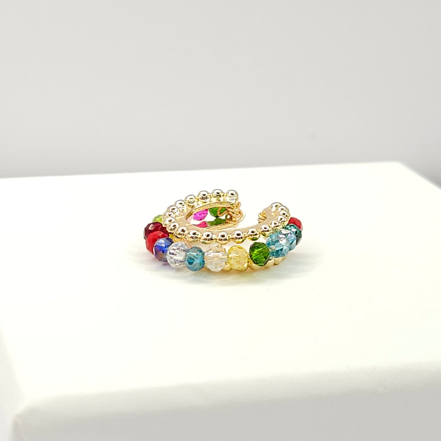 Golden ear cuff featuring an array of multicolour faceted rondelle glass beads lying on a white base