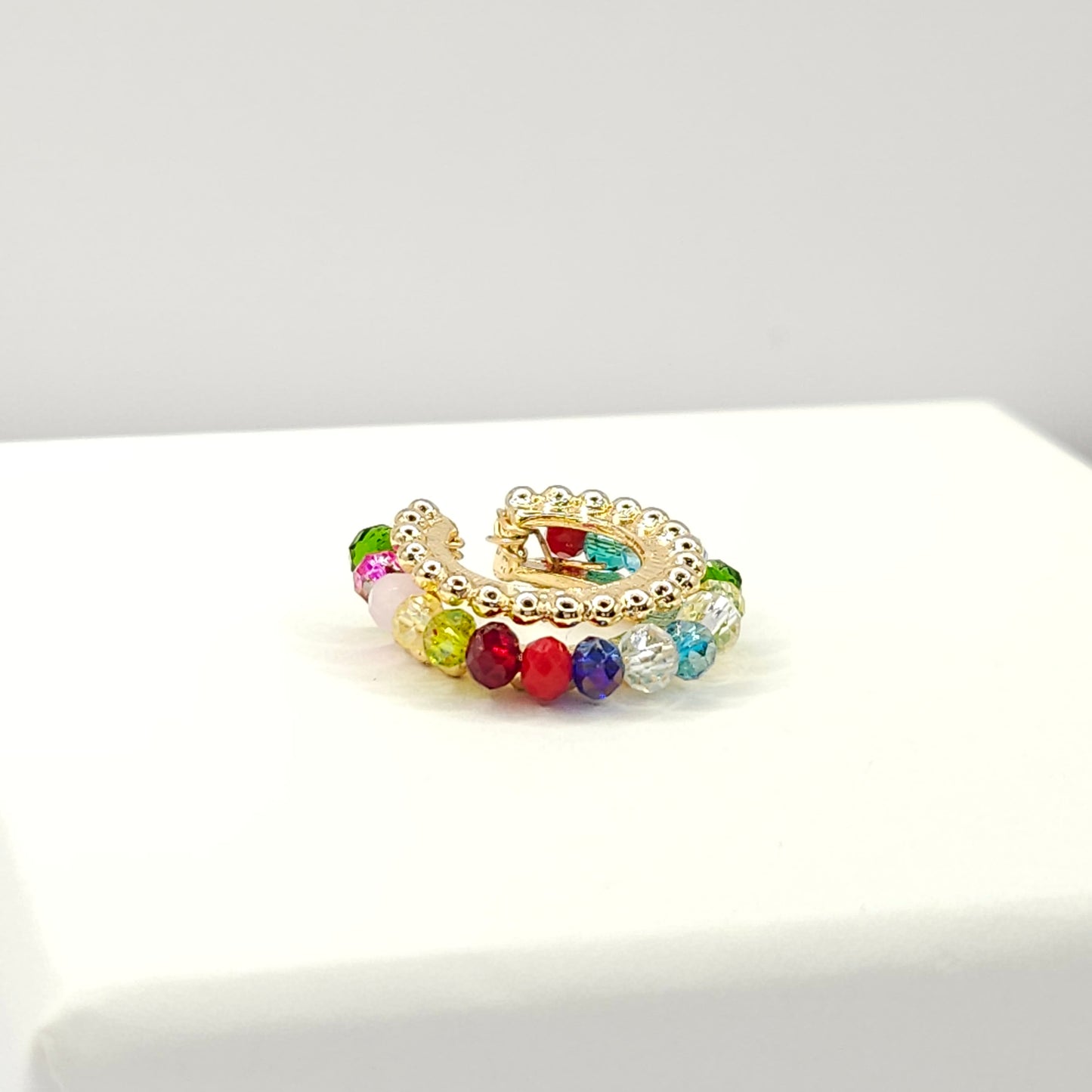 Golden ear cuff featuring an array of multicolour faceted rondelle glass beads lying on a white base