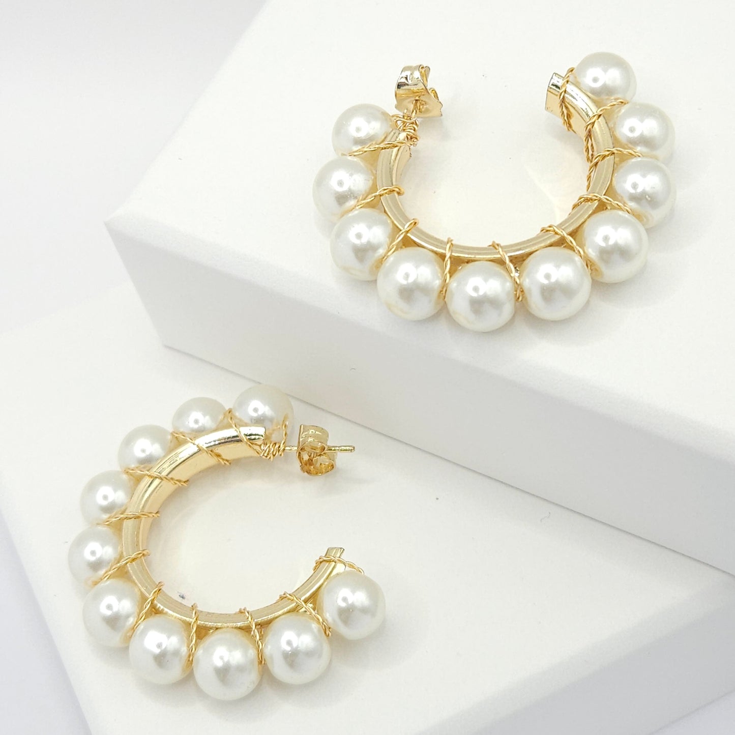 Golden hoops with a delicate weave of pearls, both lying on white bases