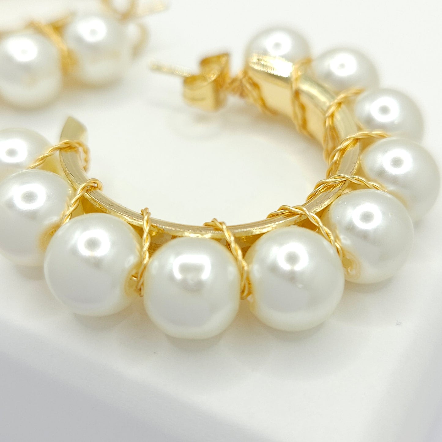 Close-up of golden hoops with white pearls, focused on lower right details, blurring towards upper left corner