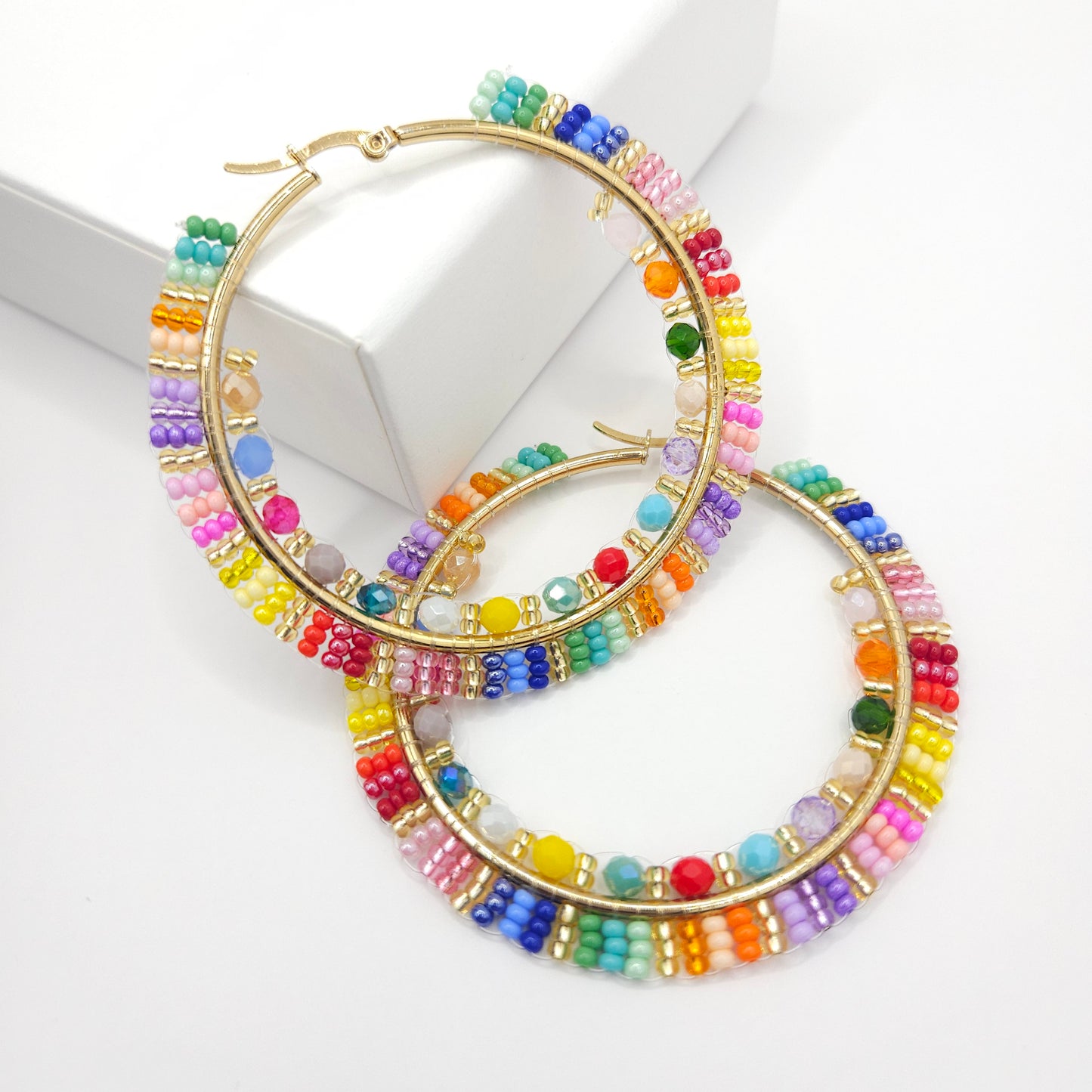 Golden hoops with colorful Czech and faceted beads, one lying on a white base, the other on a white box
