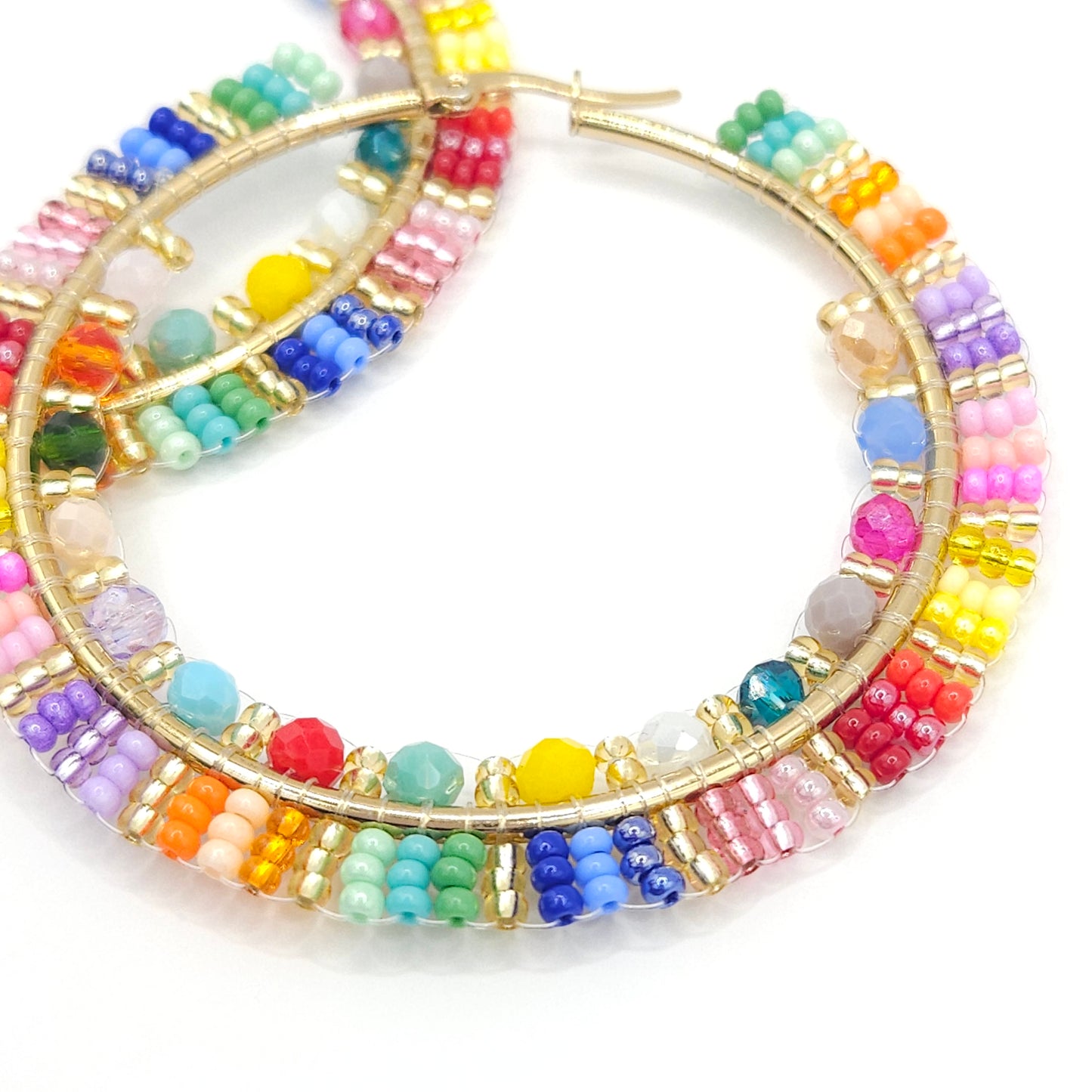 Close-up of golden hoop with colorful Czech and faceted beads, focused on lower right detail, blurring toward the upper left corner