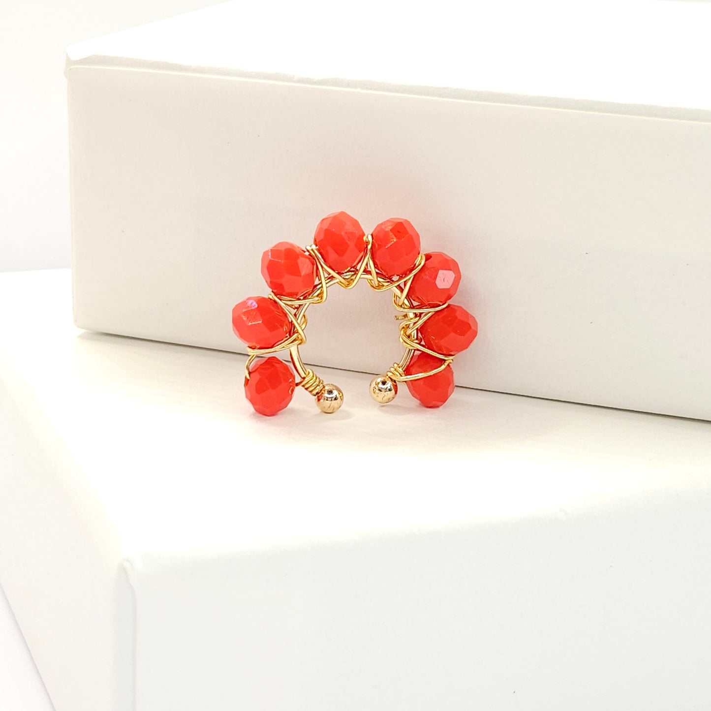 Golden ear cuff adorned with a delicate weave of red faceted rondelle glass beads standing on a white base
