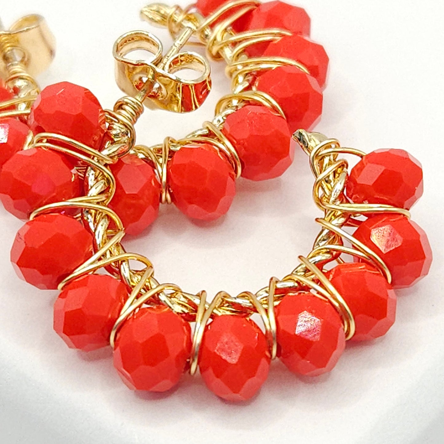 Close-up of golden hoops with red faceted rondelle beads, focused on lower right details, blurring toward upper left corner