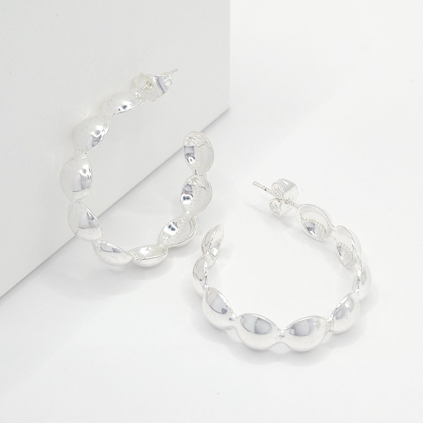 Silver hoops with flat spheres, one lying on a white base and the other standing against a white box