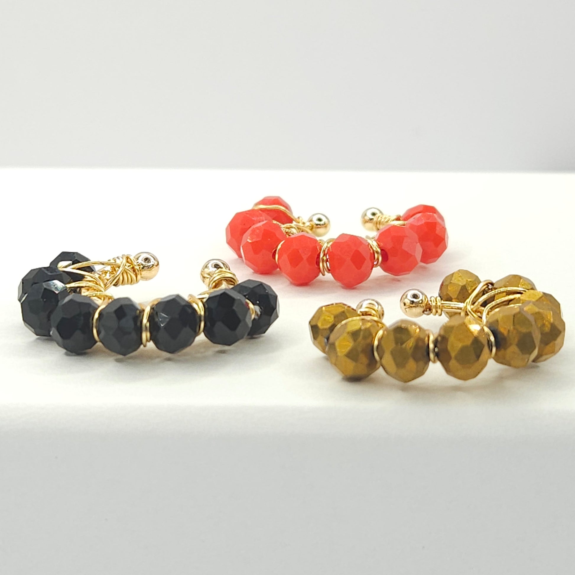 Four golden ear cuffs with faceted rondelle glass beads in black, red and chocolate, displayed on a white base