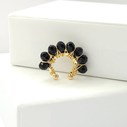 Golden ear cuff adorned with a delicate weave of black faceted rondelle glass beads standing on a white base