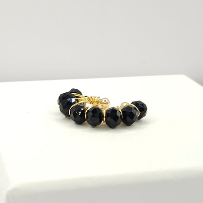 Golden ear cuff adorned with a delicate weave of black faceted rondelle glass beads lying on a white base