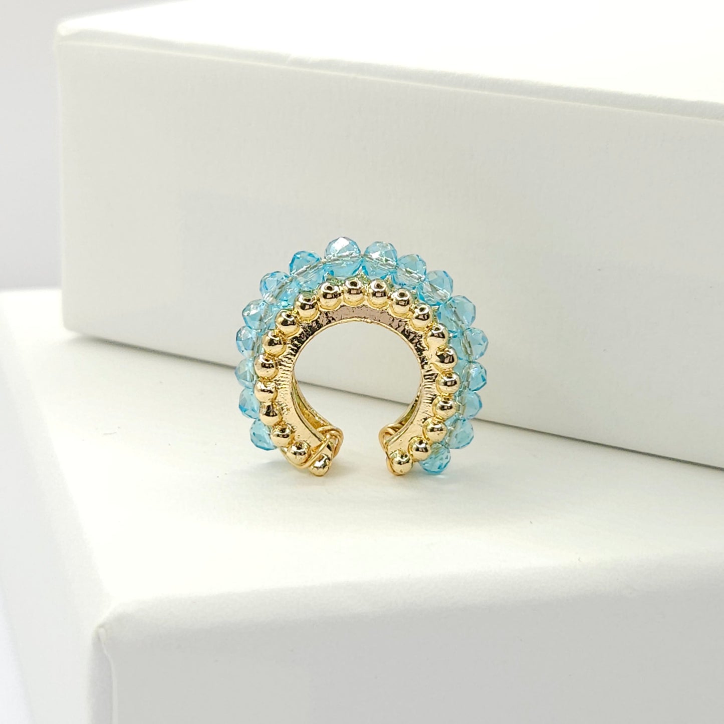 Golden ear cuff featuring an array of blue faceted rondelle glass beads standing on a white base