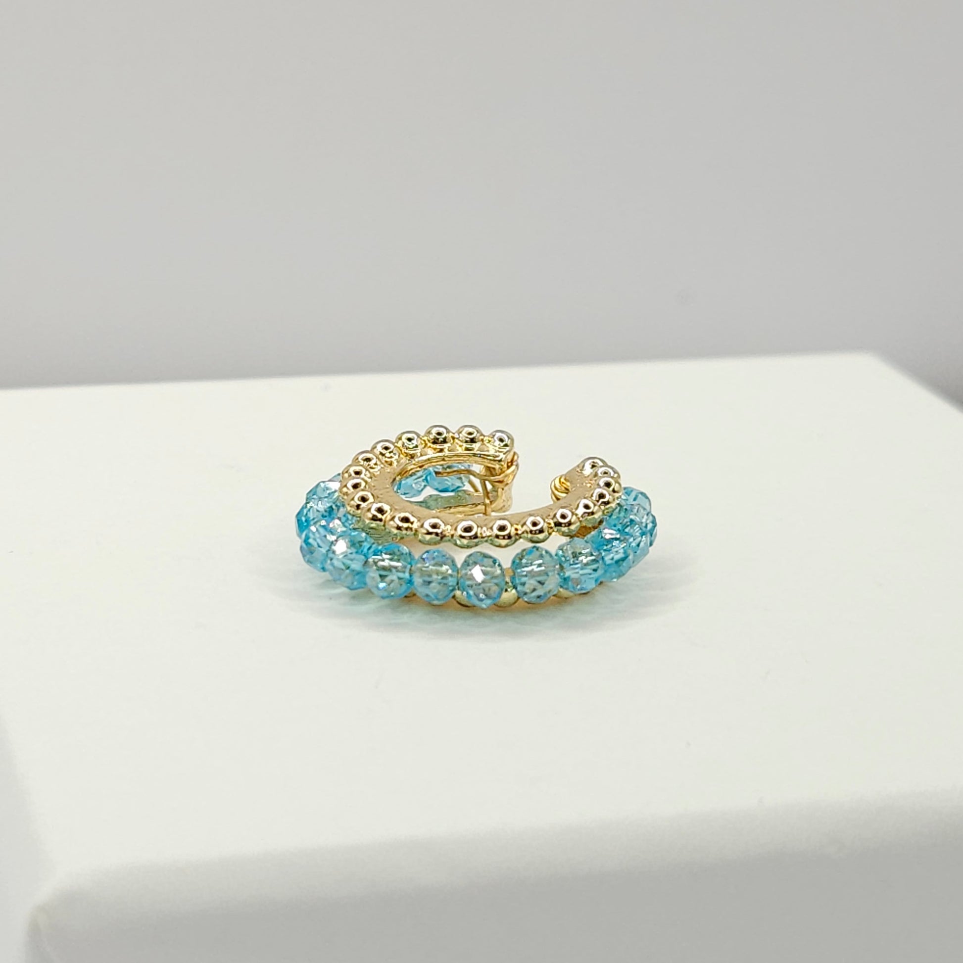Golden ear cuff featuring an array of blue faceted rondelle glass beads lying on a white base