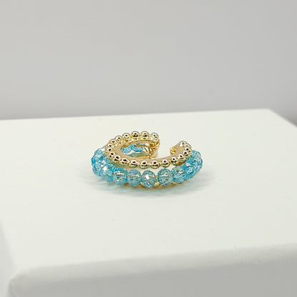 Golden ear cuff featuring an array of blue faceted rondelle glass beads lying on a white base
