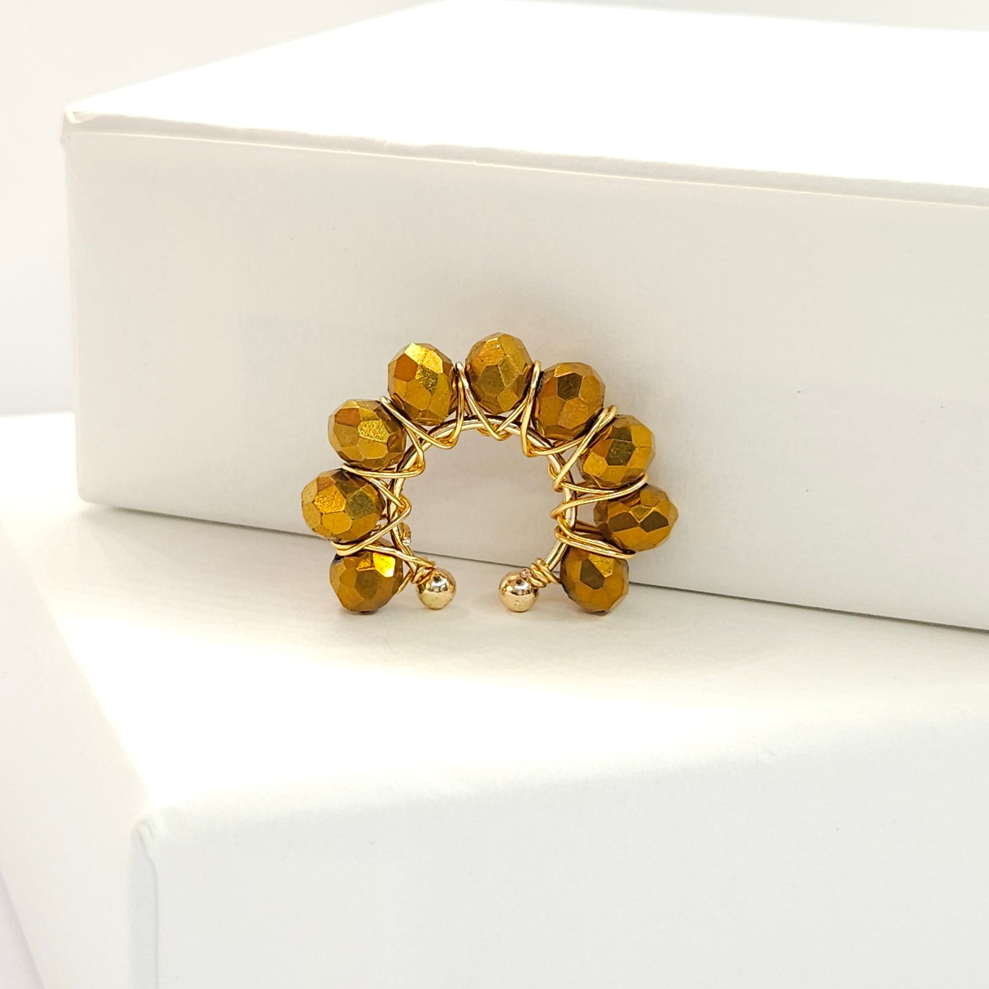 Golden ear cuff adorned with a delicate weave of chocolate faceted rondelle glass beads standing on a white base