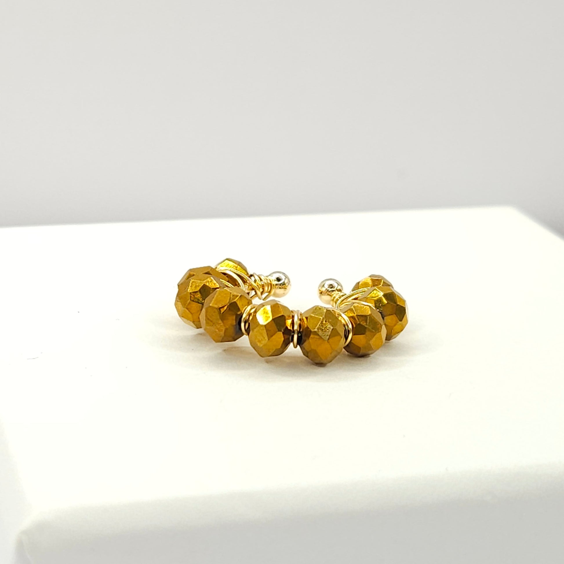Golden ear cuff adorned with a delicate weave of chocolate faceted rondelle glass beads lying on a white base