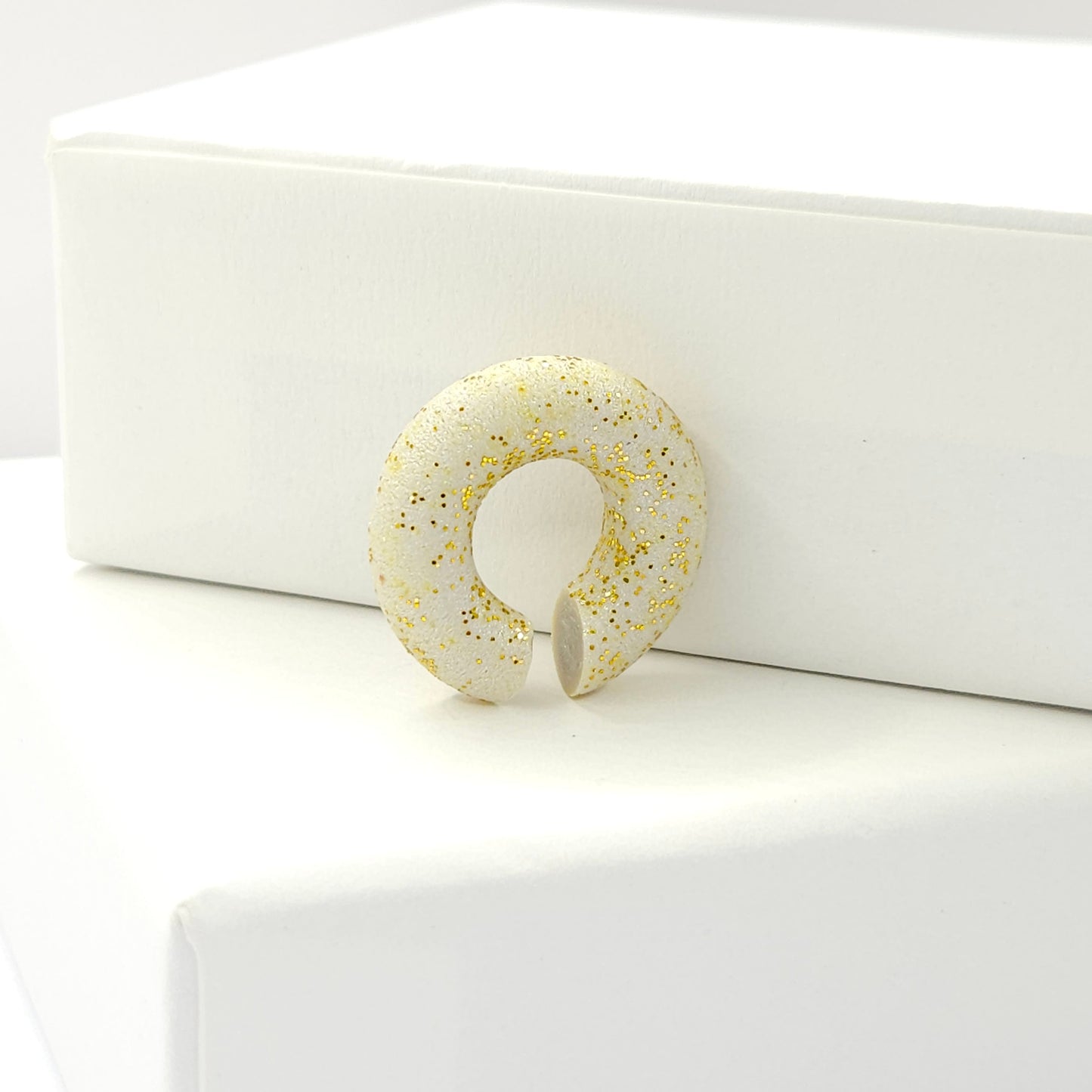 Chunky light grey ear cuff with a frosted gold finish standing on a white base