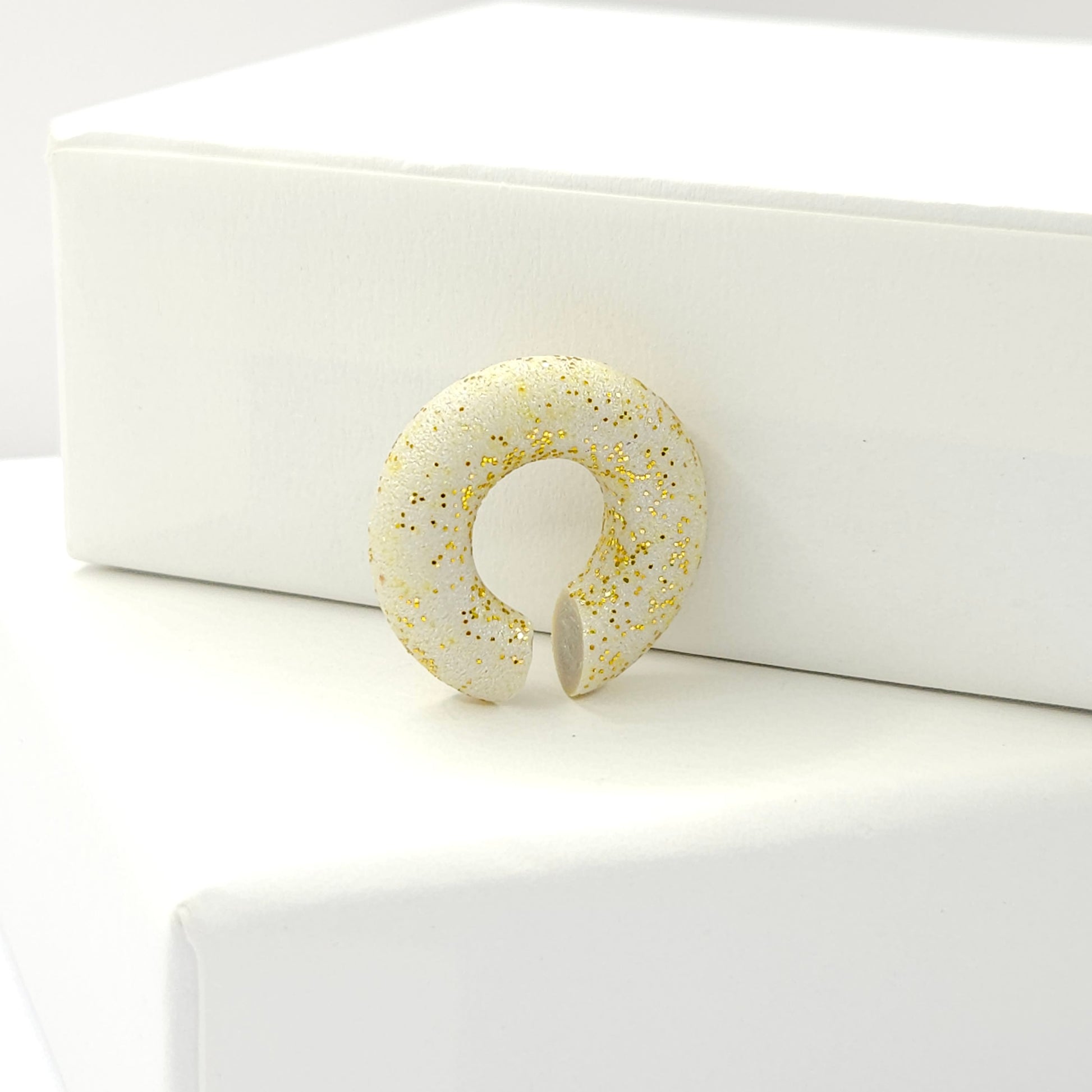 Chunky light grey ear cuff with a frosted gold finish standing on a white base