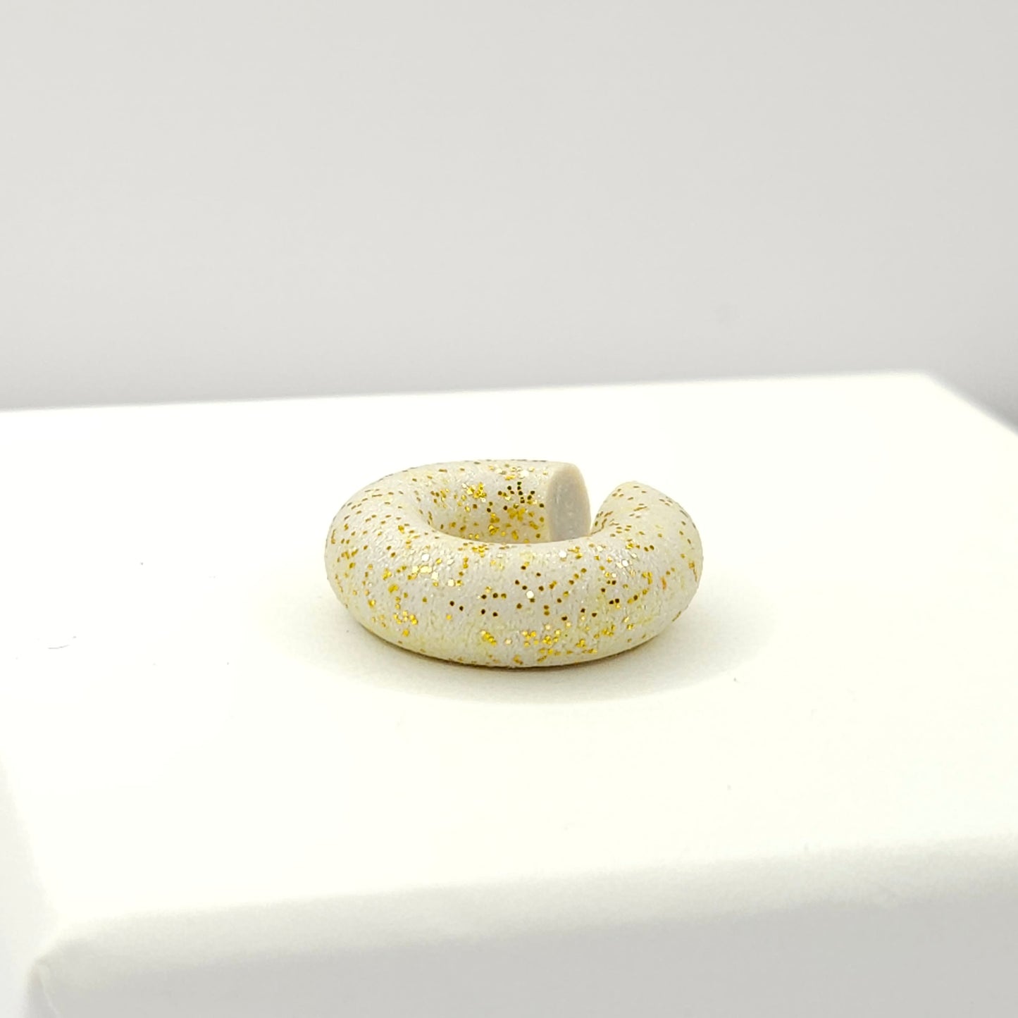 Chunky light grey ear cuff with a frosted gold finish lying on a white base