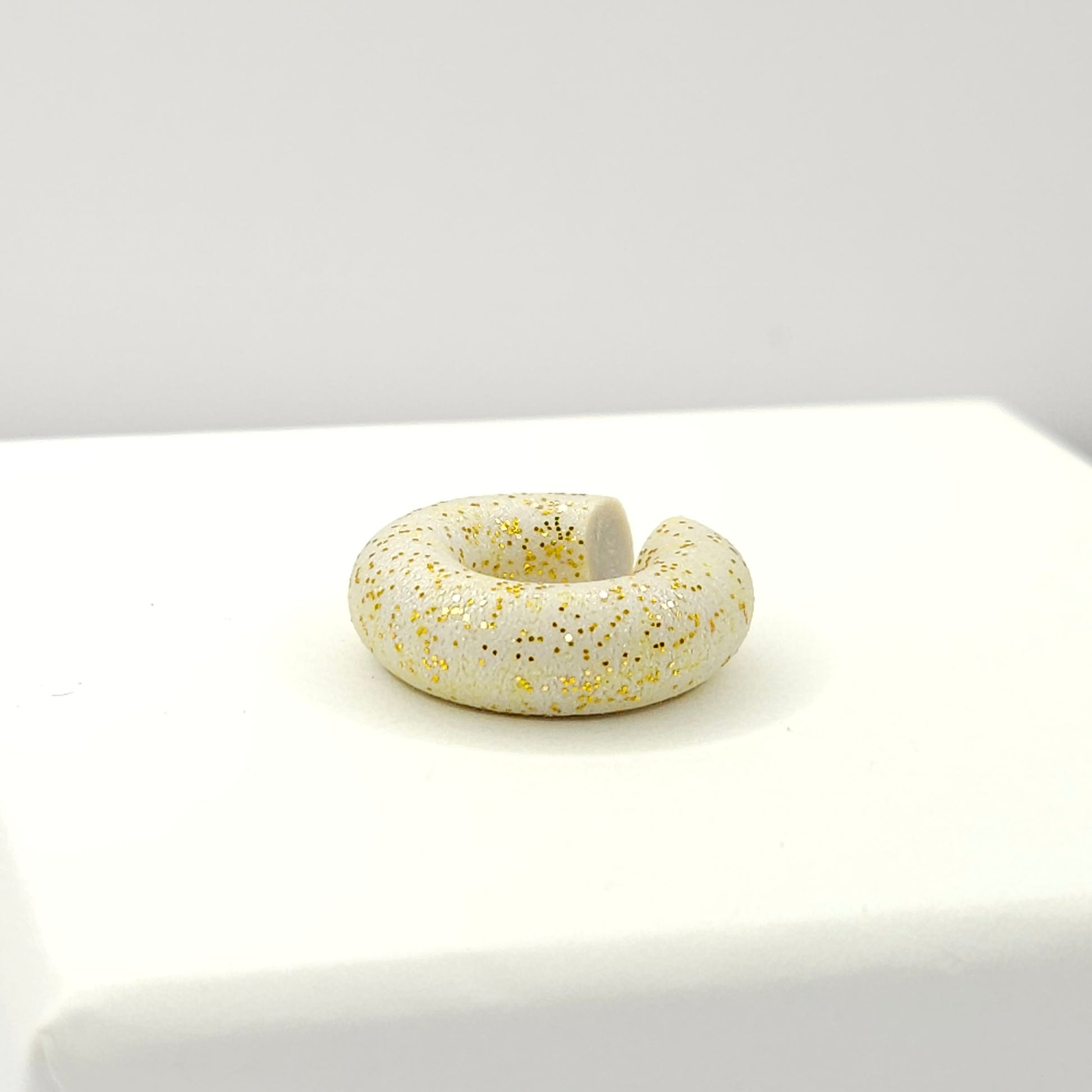 Chunky light grey ear cuff with a frosted gold finish lying on a white base