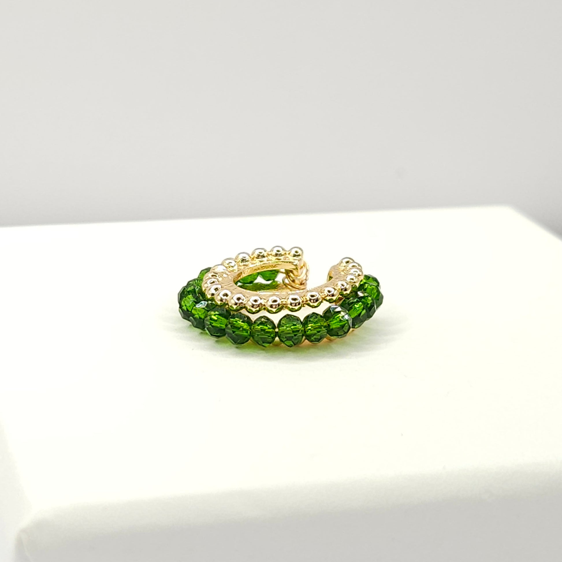 Golden ear cuff featuring an array of green faceted rondelle glass beads lying on a white base