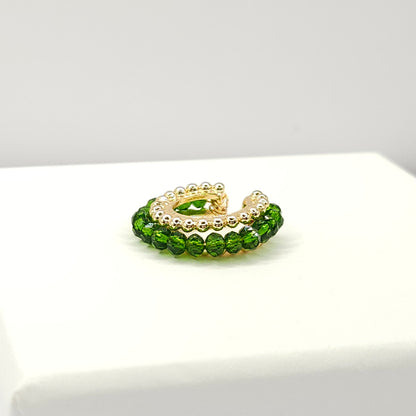 Golden ear cuff featuring an array of green faceted rondelle glass beads lying on a white base