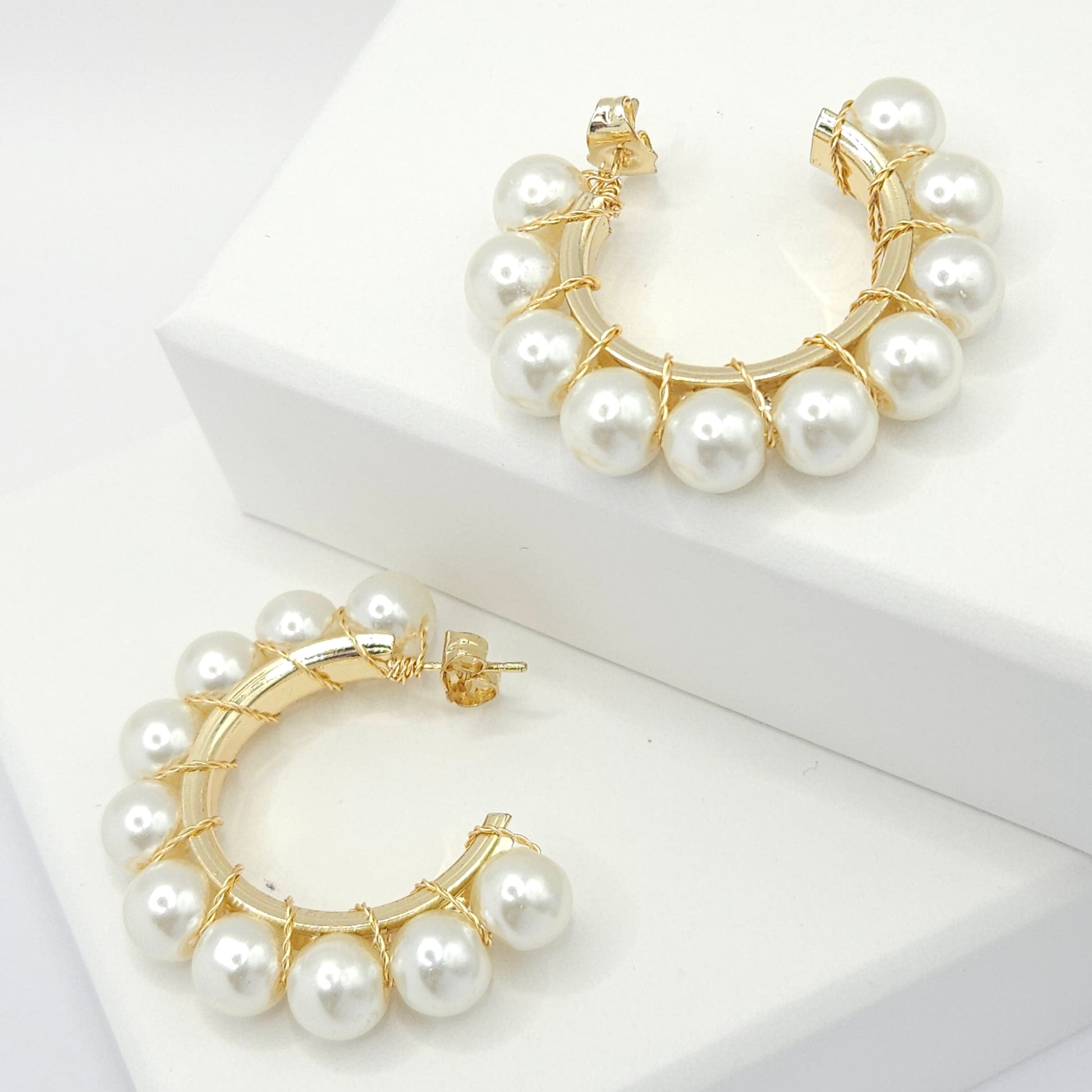 Golden hoops with a delicate weave of pearls, both lying on white bases