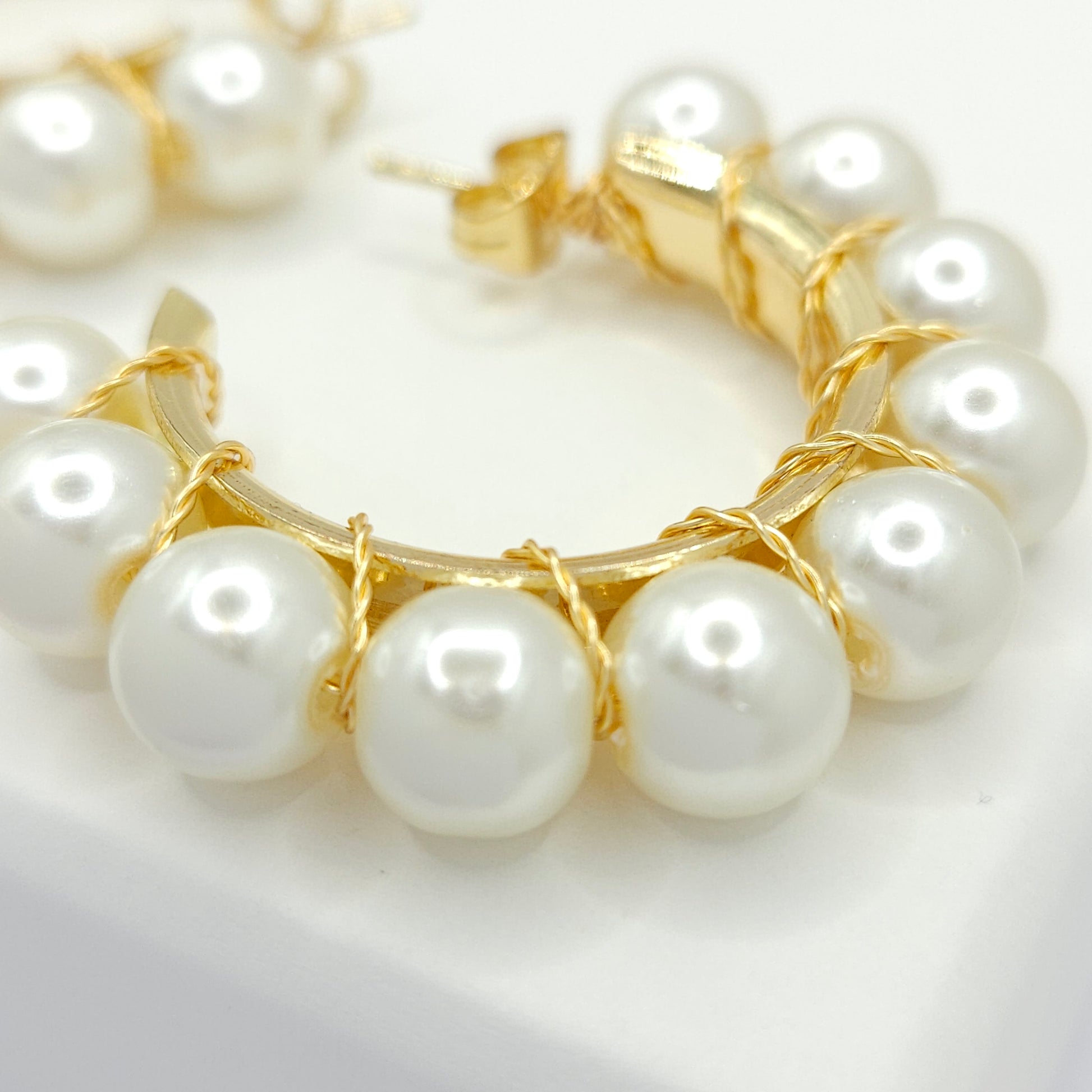 Close-up of golden hoops with white pearls, focused on lower right details, blurring towards upper left corner