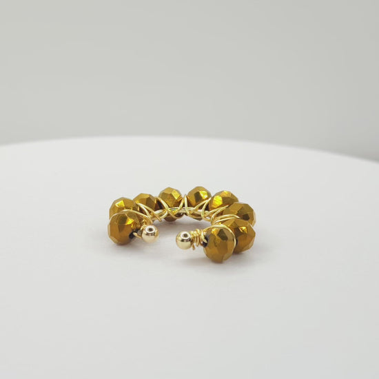 Video of a golden ear cuff adorned with a weave of chocolate faceted rondelle glass beads on a white base, rotating counterclockwise