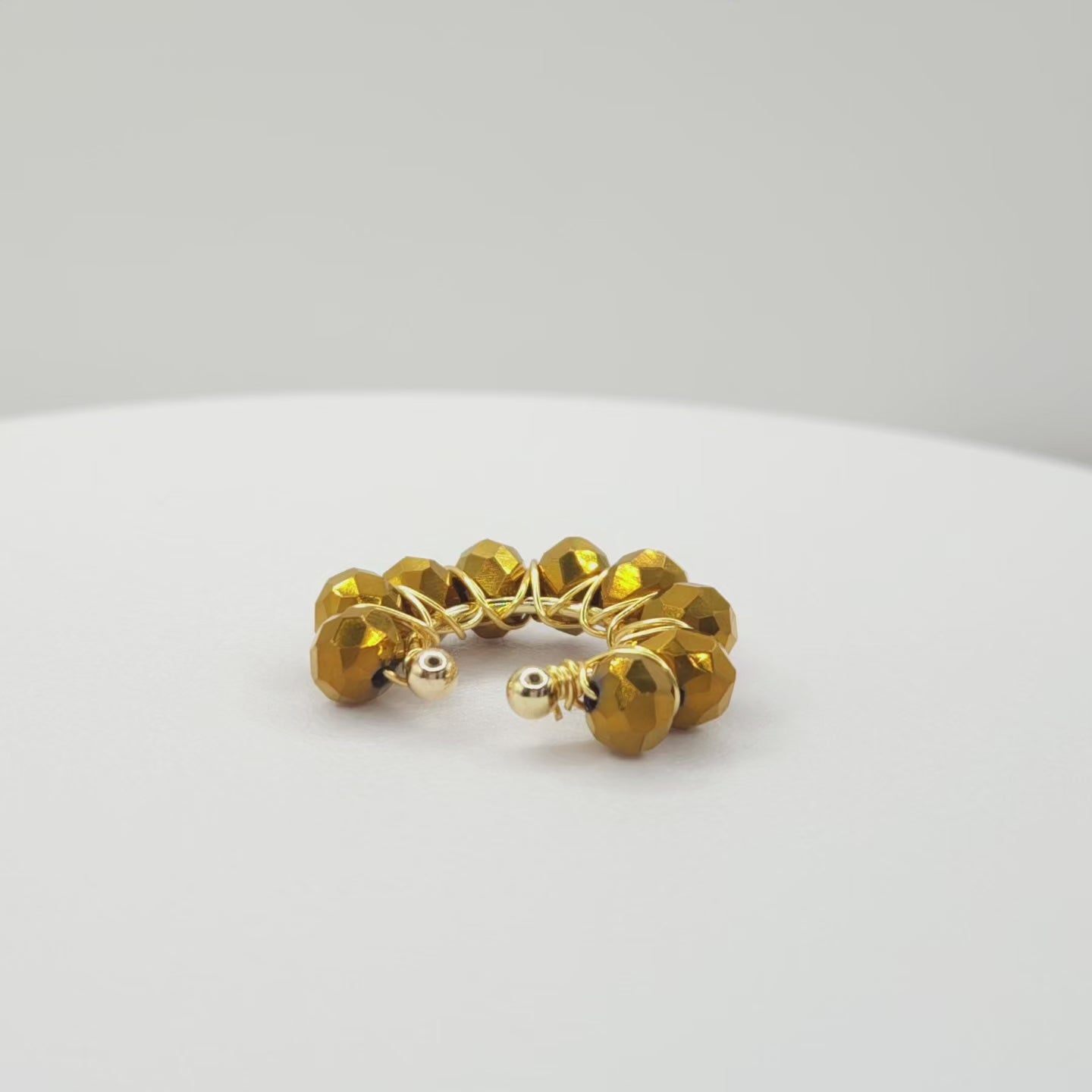 Video of a golden ear cuff adorned with a weave of chocolate faceted rondelle glass beads on a white base, rotating counterclockwise