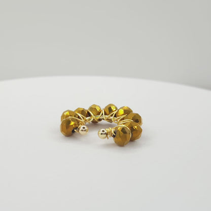 Video of a golden ear cuff adorned with a weave of chocolate faceted rondelle glass beads on a white base, rotating counterclockwise