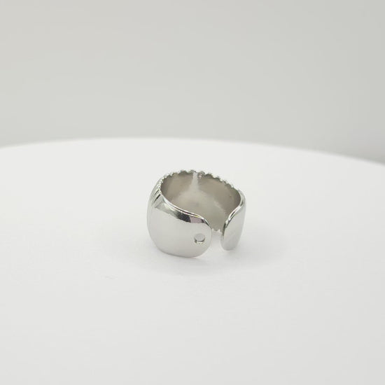 Video of a silver ear cuff adorned with subtle stripes lying on a white base