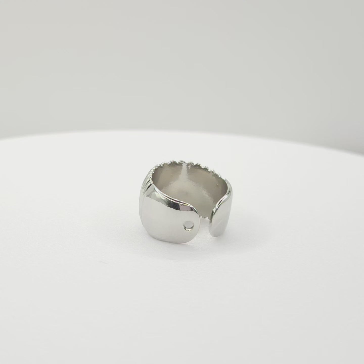 Video of a silver ear cuff adorned with subtle stripes lying on a white base