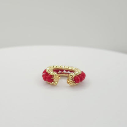 Video of a golden ear cuff featuring an array of red faceted rondelle glass beads lying on a white base, rotating counterclockwise