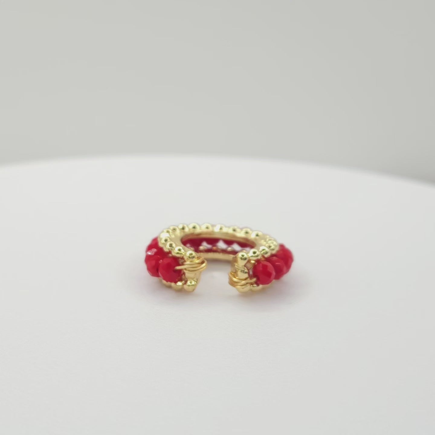 Video of a golden ear cuff featuring an array of red faceted rondelle glass beads lying on a white base, rotating counterclockwise