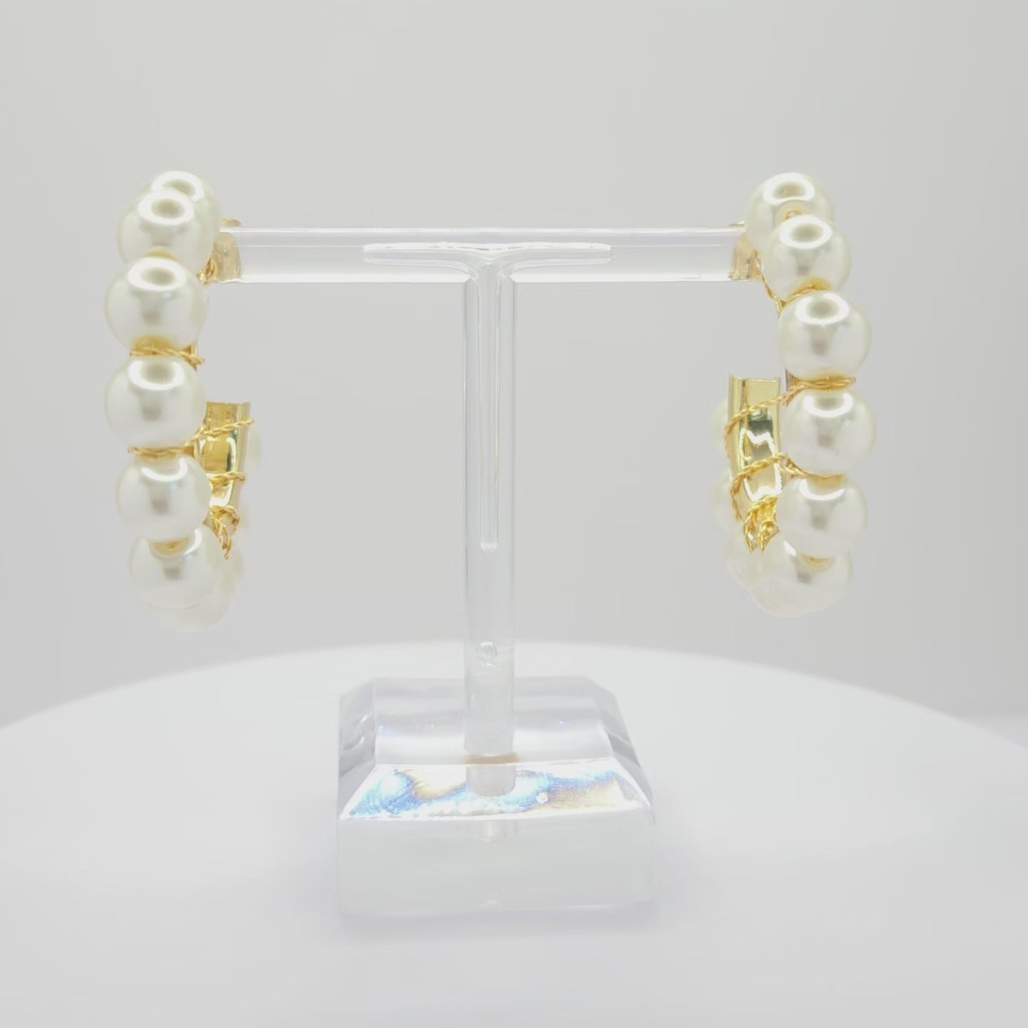 Video of golden hoops with white pearls, both standing on a white base rotating counterclockwise