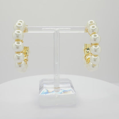 Video of golden hoops with white pearls, both standing on a white base rotating counterclockwise