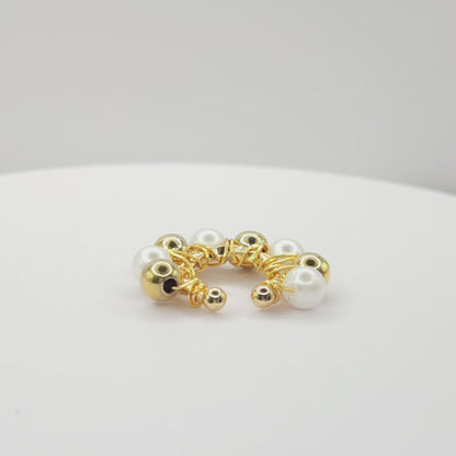 Video of a golden ear cuff adorned with golden spheres and white pearls standing on a white base, rotating counterclockwise