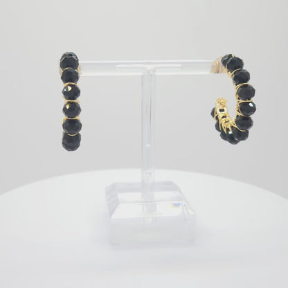 Video of golden hoops with delicate black faceted rondelle glass beads, both standing on a white base rotating counterclockwise