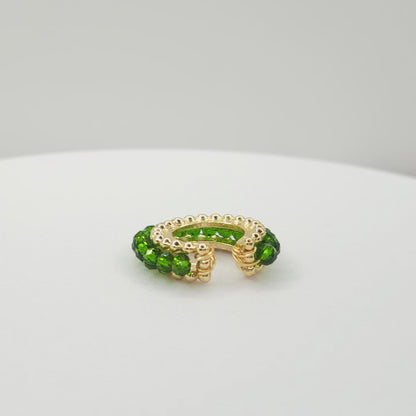 Video of a golden ear cuff featuring an array of green faceted rondelle glass beads lying on a white base, rotating counterclockwise