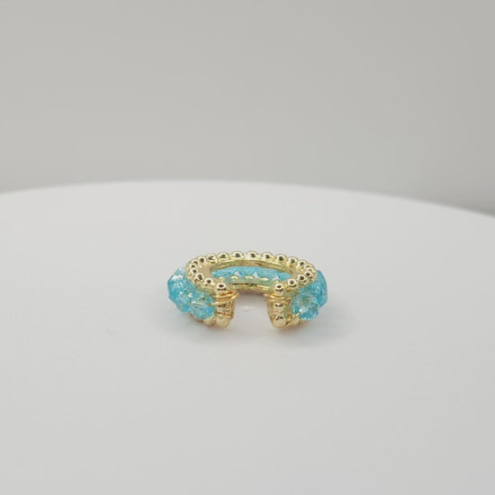 Video of a golden ear cuff featuring an array of blue faceted rondelle glass beads lying on a white base, rotating counterclockwise