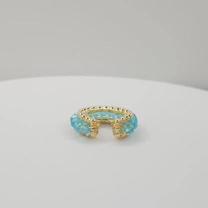 Video of a golden ear cuff featuring an array of blue faceted rondelle glass beads lying on a white base, rotating counterclockwise
