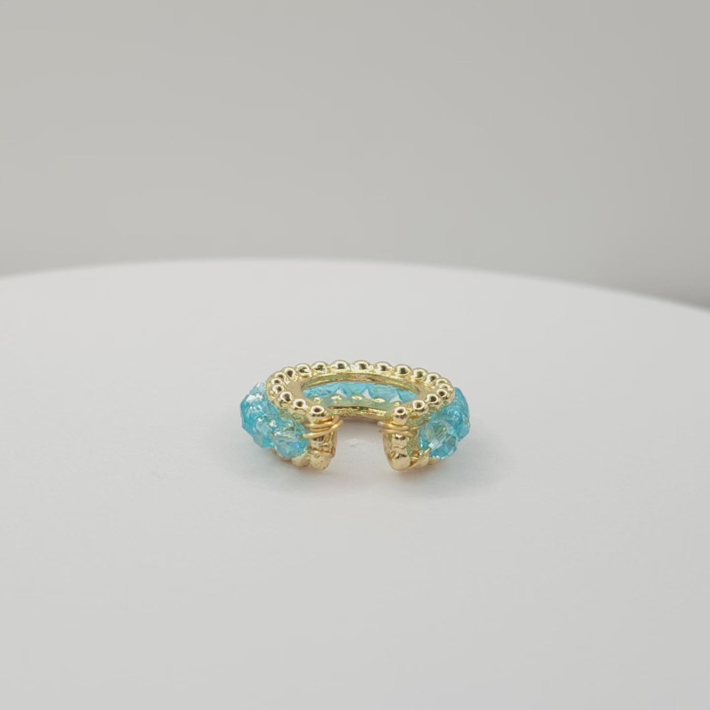 Video of a golden ear cuff featuring an array of blue faceted rondelle glass beads lying on a white base, rotating counterclockwise
