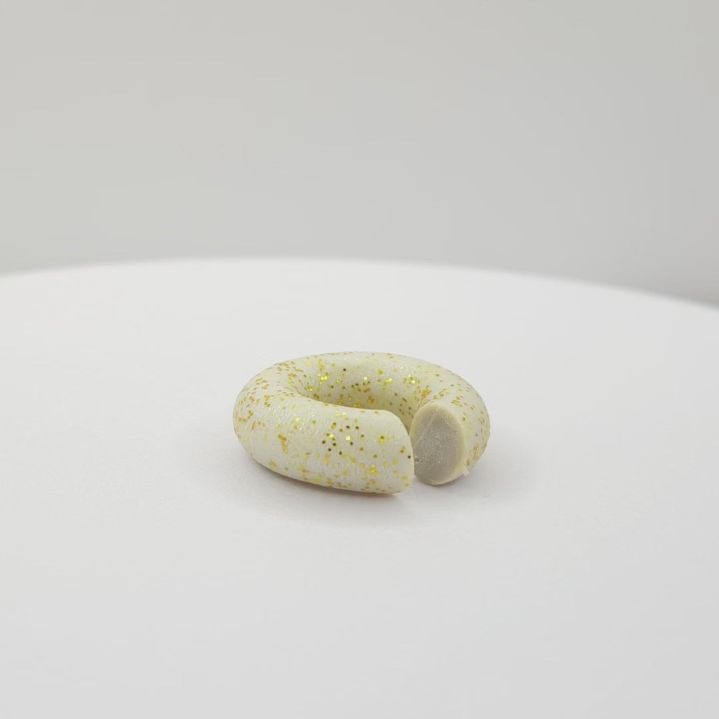 Video of a chunky light grey ear cuff with a frosted gold finish lying on a white base, rotating counterclockwise